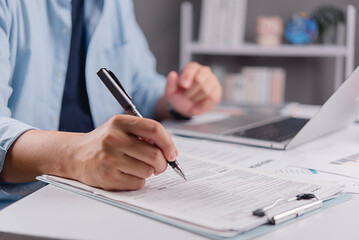 Businessman hand filling out tax return form or insurance application document. Financial paperwork, audit compliance and business contract signing concept on office desk.