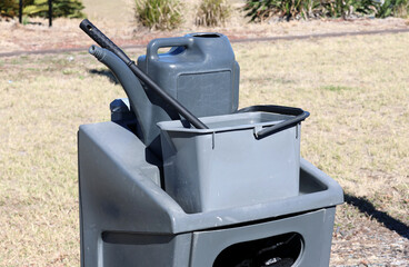Cleaning equipment consisting of a grey gray bucket with water, a squeegee and a watering can in a park