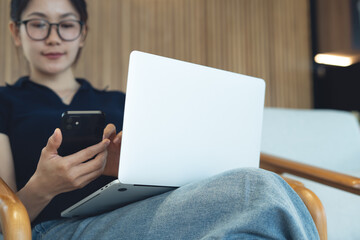 Young asian woman using mobile phone and laptop computer remote working at coffee shop. Woman using...