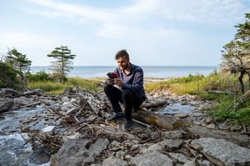 Fototapeta premium A Canadian Man Flies a drone at the Foot of a Waterfall known as “Chute à Boule” in a Forest on Anticosti Island, Quebec, Canada