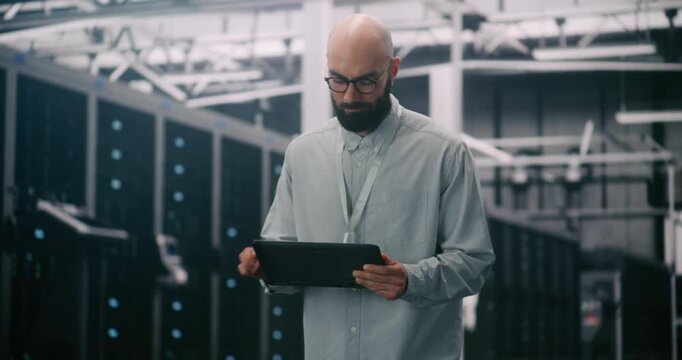 IT Professional Inspecting Racks in Data Center. Bearded Male Inspecting or Troubleshooting Equipment With Handheld Device Amidst Rows Data Servers. Concept Critical Maintenance and System Management.
