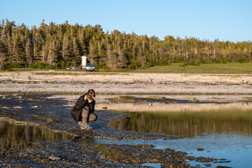 A Peruvian Woman Takes Photos with a Camera and Strolls through Baie Sainte-Claire at the Sunset, in Anticosti, Quebec, Canada