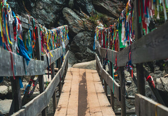 Naklejka premium Colorful ribbons adorn a wooden bridge leading to a rocky landscape in a serene outdoor setting
