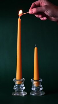 Lighting two yellow beeswax candles on a green festive background