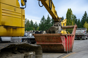 Public infrastructure construction site, excavator bucket scooping dirt out of a temporary holding sled, to backfill trench in road after installing new sewer line  © knelson20