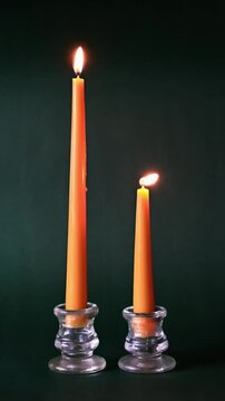 Two yellow taper candles in glass holders on a green background being blown out