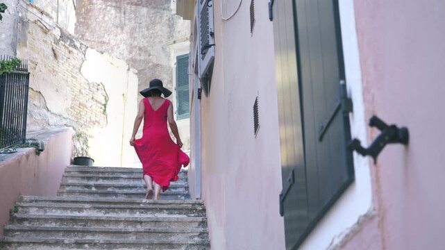Tourist travel woman in Corfu, Greece. Happy elegant fashion model in red dress enjoying vacation in old town famoust landmarks in Crofu island, Greece, slow motion