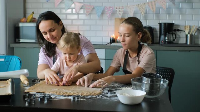 A mother and two daughters cut shapes from ginger cookie dough using small tools, creating a playful and educational baking moment filled with cooperation and warm family interaction concept