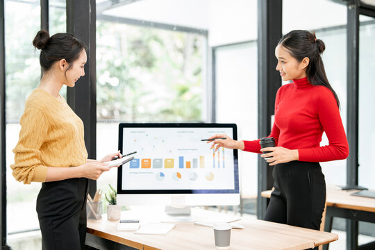 Asian business colleagues analyzing financial charts and data on computer screen in a bright modern office. - Powered by Adobe
