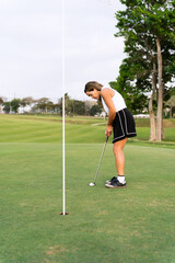 Obraz premium Young hispanic woman concentrating on putting a golf ball into the hole on a sunny golf course, enjoying an active lifestyle