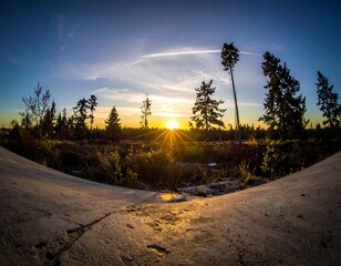Sunset over a forested bog with a sunburst and sky streaks