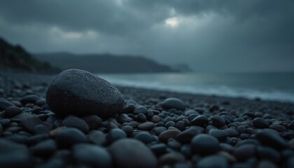 Dark, wet pebbles cover a moody beach with overcast sky. Waves gently lap shore under dramatic clouds. Coastal landscape creates somber, natural scene.