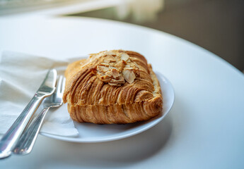 A delicious almond croissant is served on a white plate.