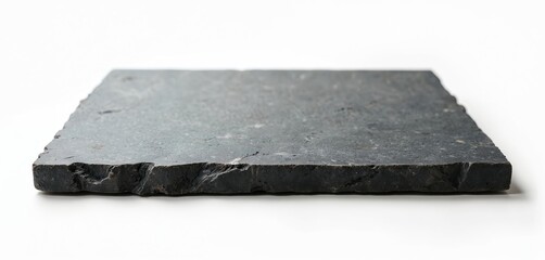 Flat dark grey slate board with rough edges rests on white surface. Rustic natural stone plate provides blank copy space for food presentation or decor.