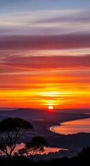 Fototapeta premium Vibrant sunset illuminates layered clouds above a silhouetted coastal landscape and water body
