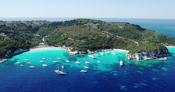 Antipaxos Island, Greece, with sandy beach, people swimming and yachts docked in the ethereal clear blue waters of the Ioanian island near Corfu