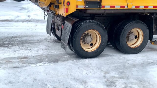 Close-up of snow plow wheels driving on an icy road after freezing rain. The scene shows the heavy machinery navigating slippery winter roads, highlighting winter maintenance, road safety, and cold cl