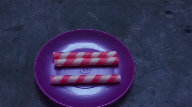 Footage of crispy wafer sticks with pink stripes, filled with sweet strawberry cream, served on a bright purple plate