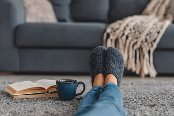 Feet resting on sofa with coffee mug and book, cozy living room, relaxation concept