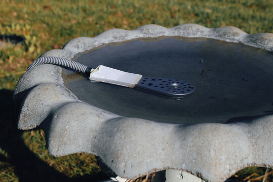 view of a de-icer being used in a concrete bird bath during the winter. lifestyles and nature design element or background 