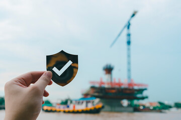 Hand holding shield icon with check mark over blurred construction site background, representing...