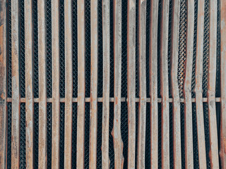 Rusty vertical metal bars form a grid with a dark mesh behind them the surface is weathered and uneven creating an industrial pattern with hints of age and decay