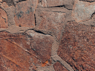 Fototapeta premium Large jagged stones are joined together with rough mortar creating a textured surface of reddish and earthy tones that looks weathered and solid with visible cracks