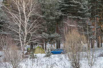 A tourist tent and car in a snow-covered winter forest. Family outdoor recreation.