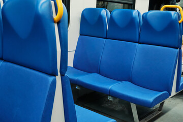 Blue vinyl seats in row, with yellow grab handle, inside an empty public transportation coach