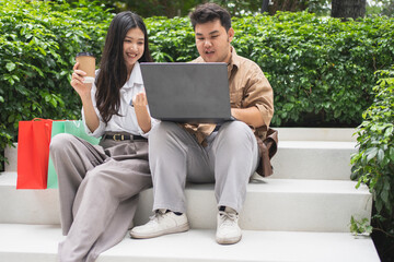 Two consumers of Asian descent walk together in a shopping mall's outdoor area. Laden with paper shopping bags, the image illustrates active participation in the retail economy and consumer gratificat