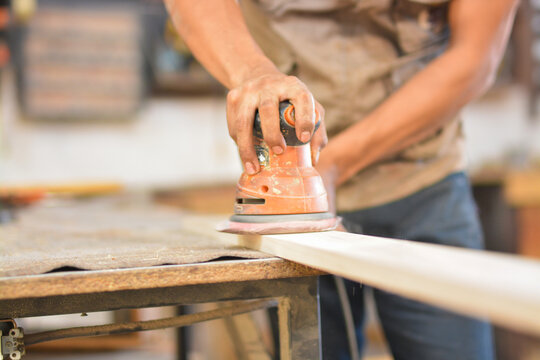 Carpenter sanding wood on a workbench. Close-up of a man using a hand sander