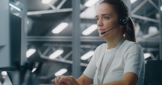 Female Engineer or Technical Support Specialist Wearing Headset and Working Console. Blue Lit, High Tech Data Center Control Room Visible Behind Her. Real Time Communication and Operational Support.