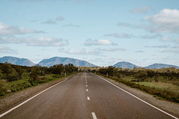 Fototapeta premium A beautiful mountain landscape with an empty asphalt road outdoor at daytime during springtime season during a road trip in Flinders Ranges in the outback of Australia with space for text.