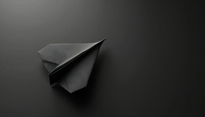 Black paper airplane poised for flight against dark backdrop. Simple origami craft symbolizes journey, imagination, and aspirational dreams of travel. Minimalist composition creates strong contrast.