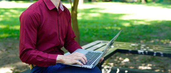 Young man working on laptop outdoors in a sunny park setting while enjoying a vibrant and...