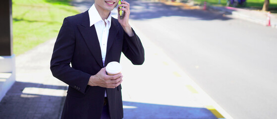 Asian businessman using smartphone while waiting for bus at bus stop