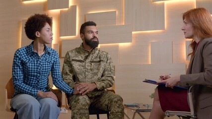 African American man soldier in military uniform and pretty black woman holding hands, visiting mature female mental health professional, trying to solve relationship difficulties during psychotherapy