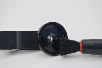 Professional cleaning of a mobile phone clip-on lens using a soft black brush, isolated on a white background. Ideal for photography maintenance and tech care concepts
