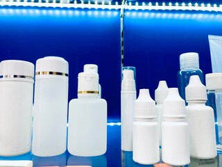 blank plastic cosmetic bottles and dropper containers on blue shelf in a pharmacy or laboratory