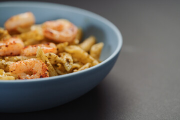 Penne pasta with shrimps and pesto in blue bowl with copy space