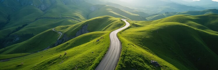 Curving asphalt road winds through vibrant green rolling hills under bright sunlight. This scenic mountain landscape offers a sense of journey and remote beauty. The open route beckons exploration.