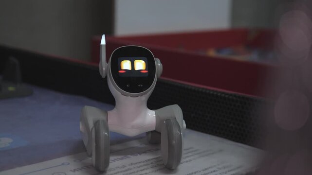 Toy Companion Robot Reacting To Touch And Petting On Tabletop Display, Warm Yellow Eyes And Small Wheels, Retail Showcase With Human Hand Interaction And Product Demo Energy