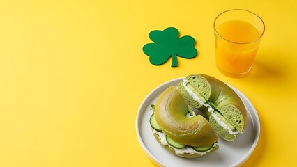 Green bagel sandwich with orange juice and shamrock on yellow background St Patrick's Day