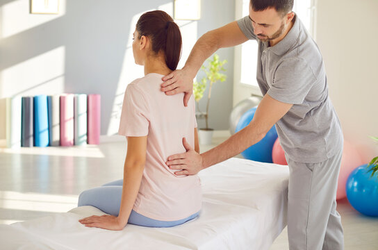 Male osteopath examining young woman in modern office. Young physiotherapist doing healing treatment on woman back in rehabilitation clinic. Chiropractor helping patient with scoliosis and back pain.