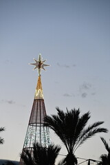 A large illuminated Christmas tree with palm trees and a Bethlehem star on top

