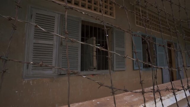 Close detail of barbed wire around former classroom cells at Tuol Sleng highlighting iron bars doors and confinement spaces, Khmer Rouge Genocide