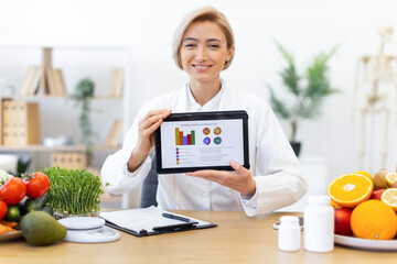 A dietitian presents a balanced diet plan on a tablet, surrounded by fresh fruits and vegetables.