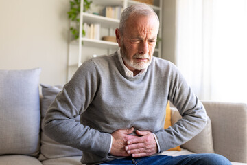 Senior man suffering from abdominal pain while sitting on sofa at home