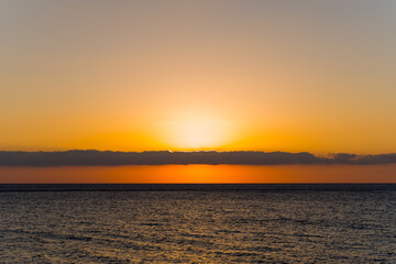 Obraz premium Minimalist seascape at Triopetra beach in Crete, featuring a glowing orange sunset above tranquil waters and a low band of clouds on the horizon.