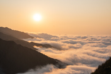 A golden sunset casts a glow over mountain peaks emerging from a sea of fluffy clouds